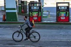 Homem de bicicleta perto de um posto de gasolina.