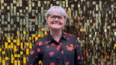 Yvonne Hughes smiles in front of a mosaic background