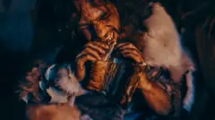 Retrato de cerca de un líder tribal vestido con piel de animal comiendo en una cueva oscura y tenebrosa por la noche.