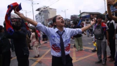 A young woman, who appears to be wearing a school uniform emblazoned with protest slogans, holds a Nepal flag as she shouts