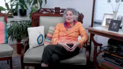 Sel Erder Yackley sentada em uma cadeira em uma sala de estar