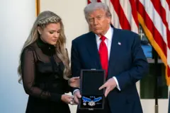 Erika Kirk, vistiendo un vestido negro de mangas largas, sostiene junto a Donald Trump, vestido de traje oscuro y corbata roja, una caja negra en la que se ve una medalla dorada con uns cinta de color azul.