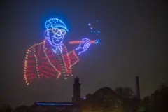 Un retrato de Hockney con sus características gafas realizado con drones en la noche.