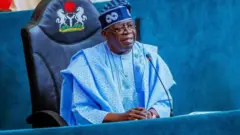Aare Bola Tinubu wọ aṣọ agbada alawọ aro pẹlu fila alawọ kan naa. O n wo ọọkan, o si n rẹrin-in musẹ bo ṣe so ọwọ rẹ mejeeji pọ