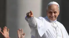 El papa León XIV sonríe y señala con el dedo a la multitud que lo aclama en la Plaza de San Pedro del Vaticano. 