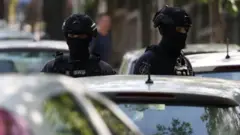 Dvojica policajaca u punoj opremi ispred automobila
