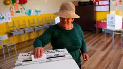 Mujer con sombrero colocando su voto en una urna en Quito, Ecuador, en el balotaje de 2023.