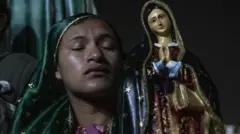 Una mujer devota, con un velo verde con bordes dorados y los ojos cerrados, ora frente a una estatuilla de la Virgen de Guadalupe