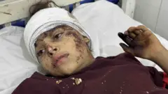 Depremde yaralanan bir kız çocuğu, kafası sargıda, sedyede yatıyor yüzünde kurumuş kan izleri var. 