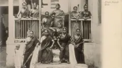 பெண் நடனக் கலைஞர்கள் அல்லது நாச் பெண்கள், 20-ஆம் நூற்றாண்டின் தொடக்கம். பம்பாயில் (தற்போது மும்பை) முதன்முதலில் ஸ்டுடியோ அமைத்த ஐரோப்பிய புகைப்படக் கலைஞர்களில் ஒருவரான எட்வர்ட் டௌரின்ஸ் இந்தப் புகைப் படத்தை எடுத்தார். இவர் மேற்கத்திய பார்வையாளர்களுக்காக நகரத்தைக் காட்சிப்படுத்தும் புகைப்படங்களில் நிபுணத்துவம் பெற்றவர்.