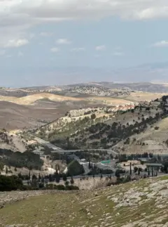 Colinas llenas de arbustos verdes y piedras, entre las que discurren calles pavimentadas.