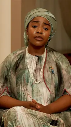 A woman sits and faces the camera