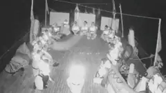 Imagem em preto e branco de baixa qualidade mostra pessoas sentadas em convés