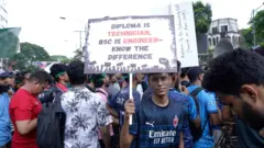 আন্দোলনকারীদের মাঝখানে একটি ফেস্টুন হাতে দাঁড়িয়ে আছেন একজন
