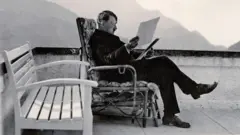 Adolf Hitler sentado em uma cadeira na varanda lendo documentos