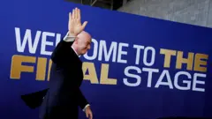 FIFA Başkanı Gianni Infantino, Dünya Kupası final maçı öncesi kameralara el sallayarak yürüyor.