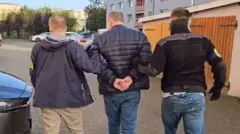 Двоє чоловіків виводять третього, який в наручниках стоїть між ними