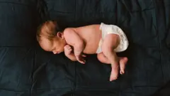 Un bebé a pocos días de nacido duerme en pañales sobre un fondo oscuro