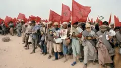 مغاربة يحملون صور الملك الحسن وأعلام المغرب أثناء المشاركة في المسِيرة الخضراء
