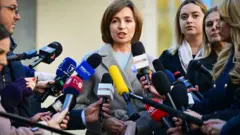 A presidente da Moldávia, Maia Sandu (centro), fala à imprensa após votar nas eleições presidenciais em uma seção eleitoral em Chisinau, em 3 de novembro de 2024. Maia Sandu tem cabelos castanhos curtos e veste um elegante casaco cinza.