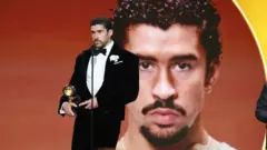 Bad bunny sahneden ödülüyle, arkada da büyük boy bir fotoğrafı var yakın plan. 