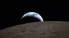 Earth poking out from behind the cratered surface of the Moon.