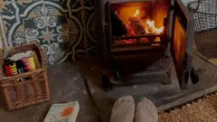 Камін на дровах, книга та ноги в шкарбетках перед ним