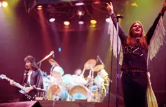 Ozzy Osbourne com os braços no ar no palco com Tony Iommi em 1976