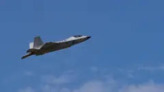 青空を背景に、灰色の戦闘機が左から右へと飛んでいる