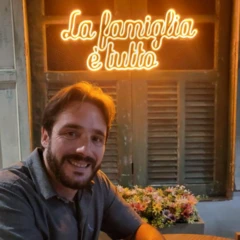 Dono de restaurente italiano sorri em frente de um painel luminoso que diz: La familgia é tutto