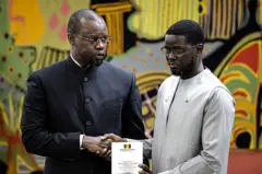 Le Premier ministre sénégalais Ousmane Sonko (à gauche) remet au président sénégalais Bassirou Diomaye Faye (à droite) le rapport officiel sur le massacre de Thiaroye lors d'une cérémonie au palais présidentiel de Dakar, le 16 octobre 2025. 