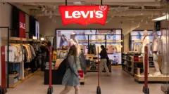 Mulher anda em uma loja da Levi's, onde diversos tipos de roupas são exibidos em prateleiras