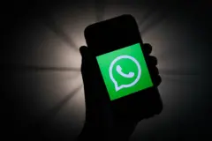 Qara fonda bir əldə telefon tutulub, telefonda WhatsApp loqosu görünür.