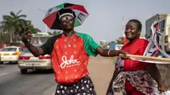 Deux partisans de John Mahama posent au bord de la route pour une photo à Accra le 3 décembre 2024. L'un d'eux porte l'emblème du Congrès démocratique national - un parapluie - en guise de chapeau.