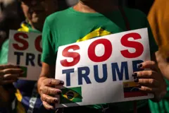 Mulher carregando um cartaz escrito SOS Trump e usando uma blusa do Brasil