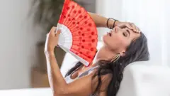 Mulher sentada em sofá se abandando com leque