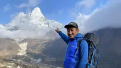 El Dr. Nima Namgyal Sherpa, vestido con un jersey azul, una gorra negra y llevando una mochila negra, señala con el dedo hacia el monte Ama Dablam en la región del Everest.
