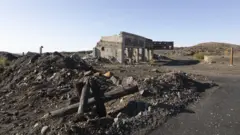 Un edificio en ruinas sobre un terreno pedregoso, bajo un cielo azul