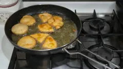Vista de cima de pastéis sendo fritos em uma frigideira, em uma cozinha doméstica