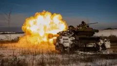 Uma grande explosão com chamas brancas e laranja sai de um tanque ucraniano, disparando contra posições russas em um cenário coberto de neve na região de Donetsk, em janeiro de 2024