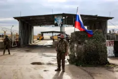 Silahlı bir militan, Rusya bayrağı ve Putin'in resmi önünde