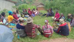 Abagore n'abagabo bicaye mu byatsi bakoze uruziga, harimo n'abafite amakayi n'amakaramu, mu karere ka Nyamagabe, mu majyepfo y'u Rwanda