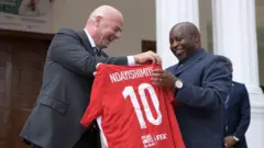 Umukuru wa FIFA Gianni Infantino (ibubamfu) na Perezida w'u Burundi Evariste Ndayishimiye baseka bafashe umupira wo gukinana wanditseho Ndayishimiye na nimero 10
