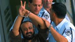 مروان برغوتی، رهبر جنبش فتح یاسر عرفات در کرانه باختری، با دستبند و انگلشتش به علامت پیروزی، در ۲۹ سپتامبر ۲۰۰۳ در راه بازگشت به زندان پس از حضور در دادگاه تل آویو،در کنار خودروی پلیس اسرائیل 