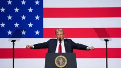 ABD Başkanı Donald Trump, 30 Eylül'de dev bir Amerikan bayrağının önünde bir kürsüde konuşma yapıyor. Kollarını havaya kaldırmış ve kendisini dinleyen generallere sesleniyor.