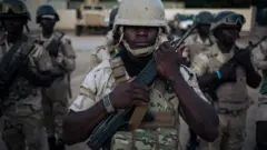 Des soldats procèdent quotidiennement à la cérémonie de descente du drapeau dans le secteur n°1 de la Force Multinationale Mixte (FMM) basée à Mora, dans la région de l'Extrême Nord du Cameroun.