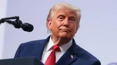 Trump mira con una medio sonrisa, viste traje azul marino y corbata rojo oscuro, con camisa blanca.