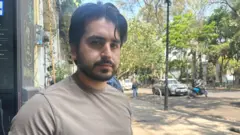 Miguel Alfonso Meza, vestindo uma camiseta cinza, olha para a câmera enquanto está na calçada de uma rua na Cidade do México