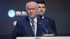 Devlet Bahçeli lacivert ceketli bir kürsüde konuşuyor. 