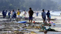 People walk through debris along the shoreline of Patong beach of Phuket island, southern Thailand, 27 December 2004